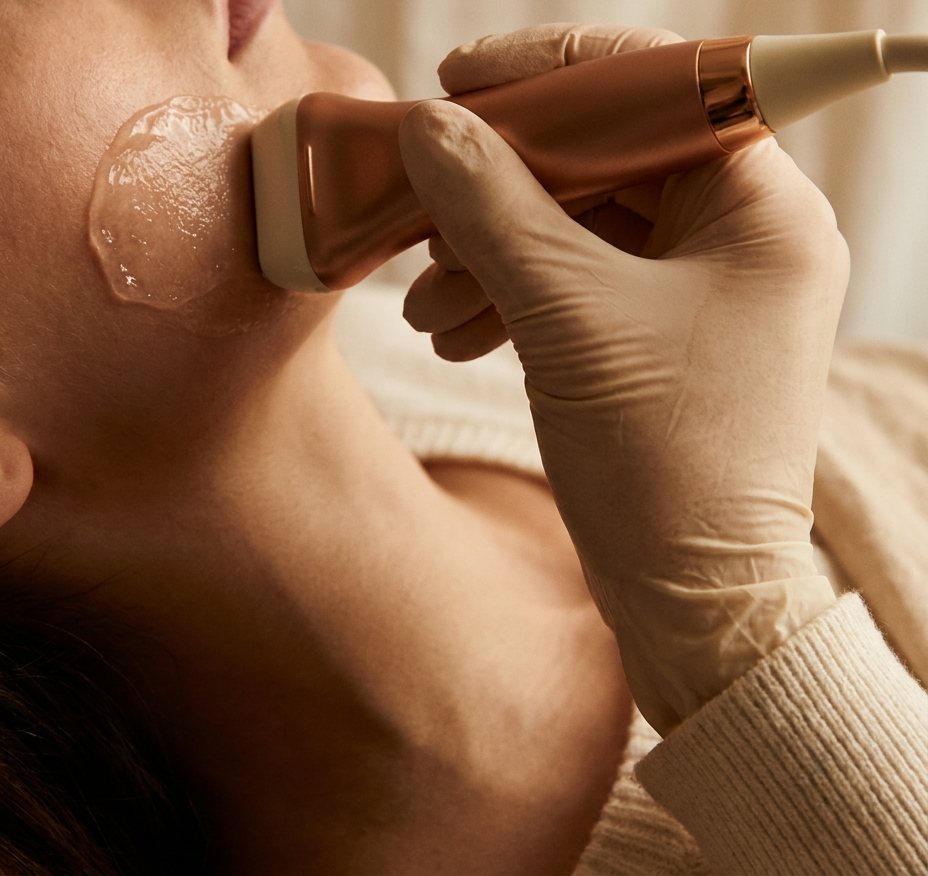 Mão com luva segurando um transdutor linear pequeno sobre a bochecha, com gel na pele